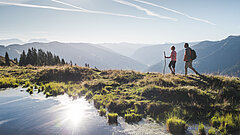 Wanderpaar am Berg mit kleinem Bergteich, dahinter Tallandschaft.