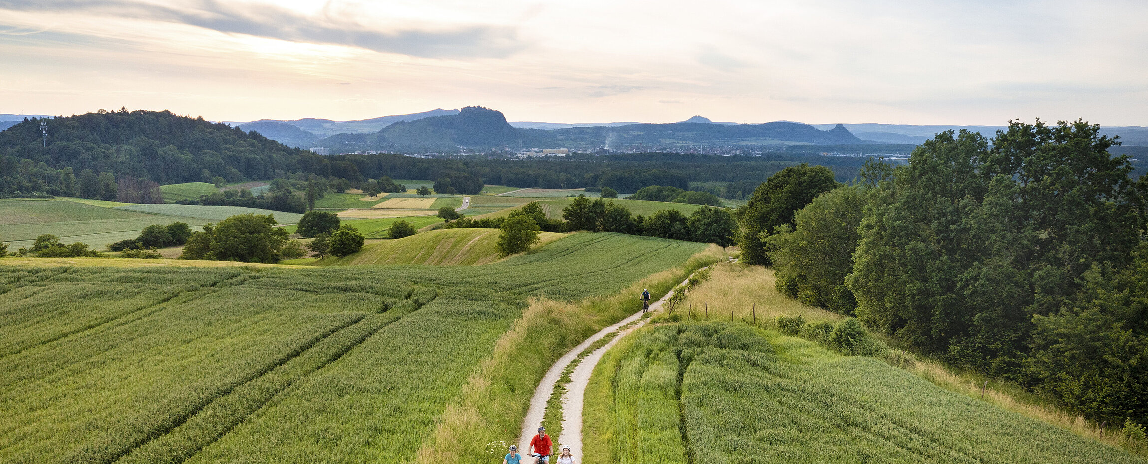 zwei Radler fahren zwischen Feldern unter blauen mit Wolken durchzugenem Himmel